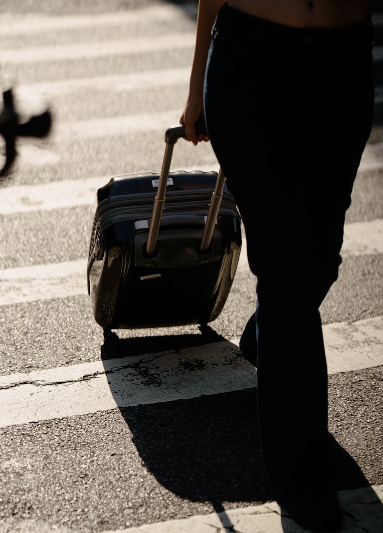 Close-up of a Person Walking with a Suitcase on a Street Crossing