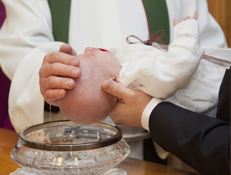 A baby being baptized during a ceremonial Christian baptism, featuring a priest and holy water.