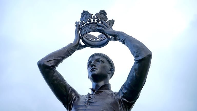Bronze statue of a figure holding a crown aloft, located outdoors in Warwickshire, England.