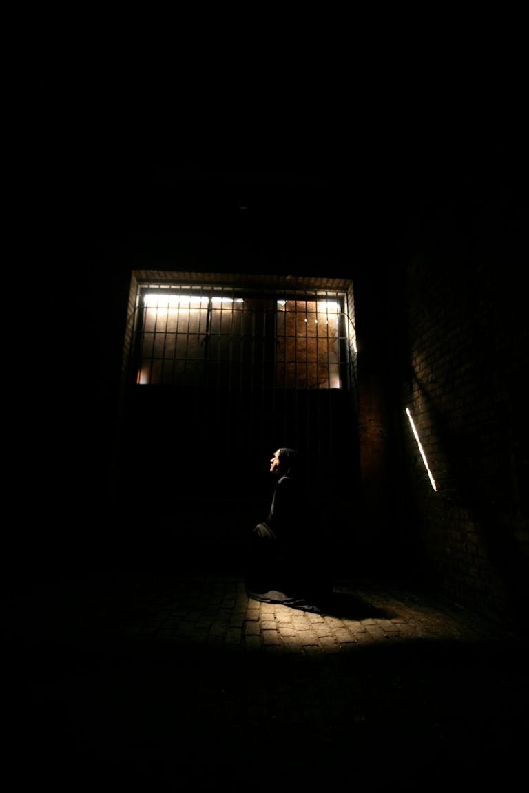A mysterious silhouette of a man in a dimly lit room with bars and dramatic shadows.