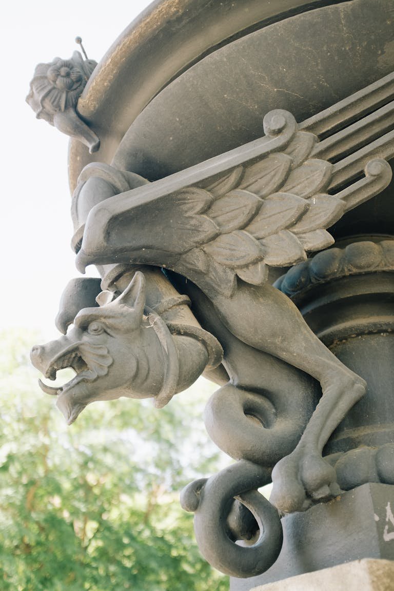 Close-up of a detailed stone gargoyle with wings on a sunny day.