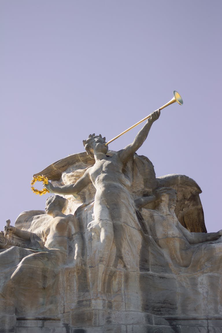 Sculpture of an angel playing a trumpet, captured from a low angle.