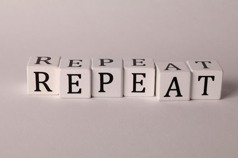Wooden blocks arranged to spell 'REPEAT' on a neutral background.