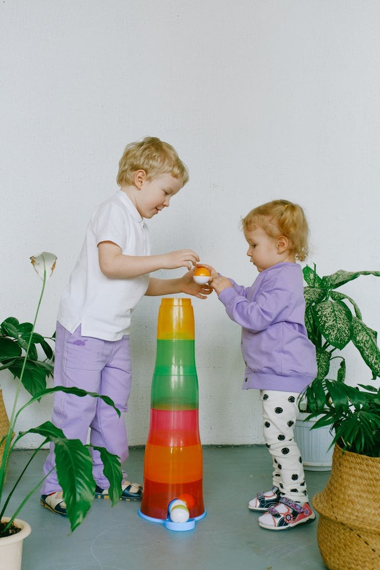Two children enjoy playful learning with colorful stacking cups indoors surrounded by plants.