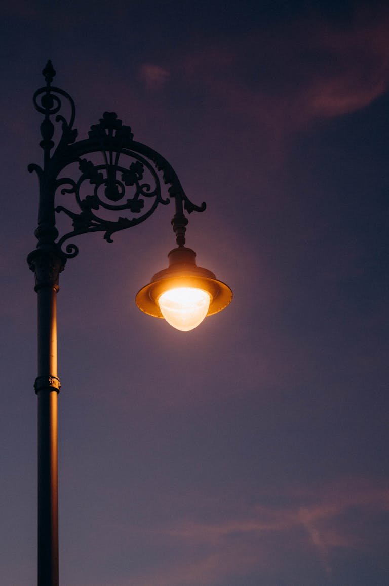 A vintage iron street lamp gleams warmly against a deep twilight sky, evoking urban nostalgia.