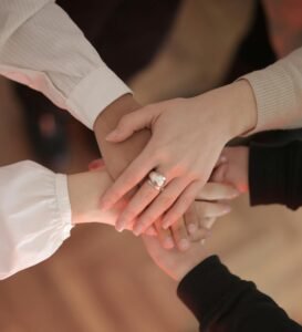 Top view of faceless friends in different clothes stacking hands together while standing on wooden floor indoor on sunny day