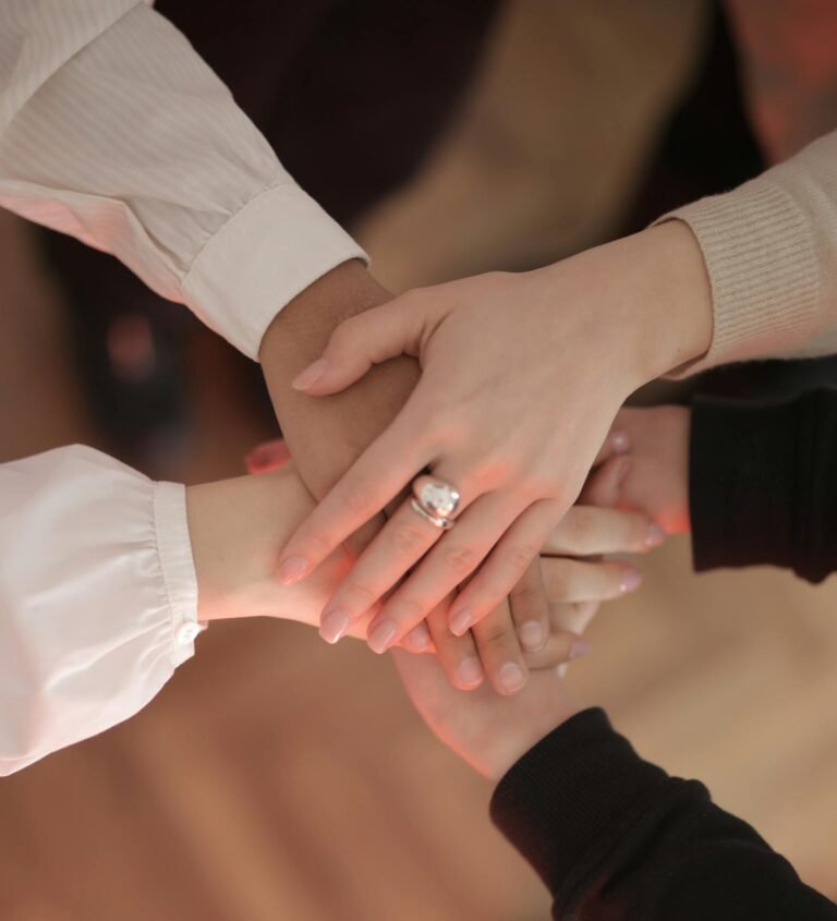 Top view of faceless friends in different clothes stacking hands together while standing on wooden floor indoor on sunny day